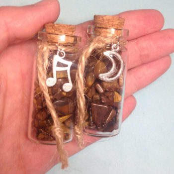 A glass jar with a cork, containing Tiger's Eye crystal chips, with a charm on twine around the top of the bottle
