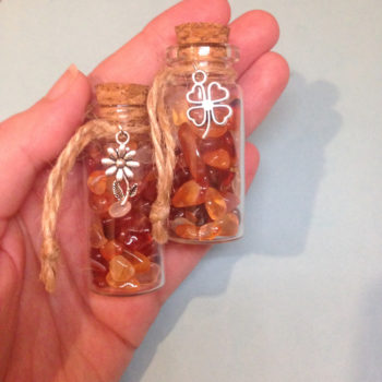 A glass jar with a cork, containing carnelian crystal chips, with a charm on twine around the top of the bottle
