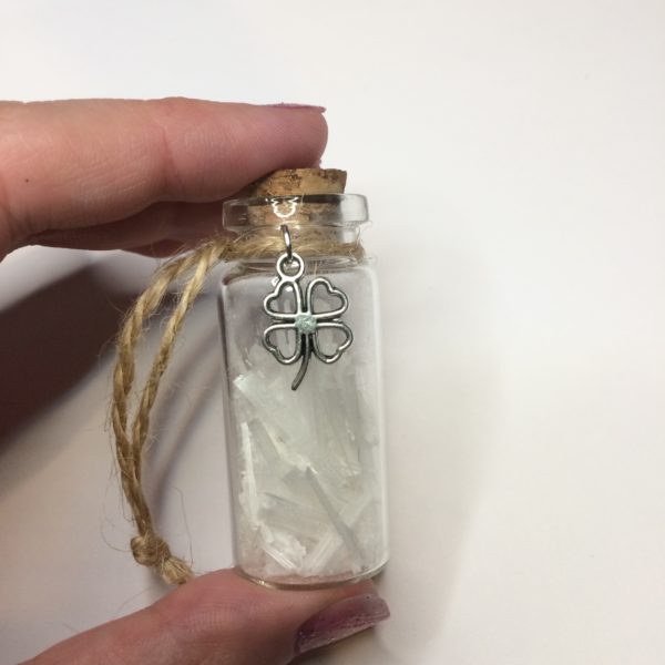 A glass jar with a cork, containing selenite crystal chips, with a charm on twine around the top of the bottle