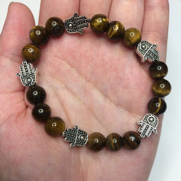 A woman's hand holding a brown Tiger's Eye gemstone bead bracelets with five silver Hand of Fatima beads